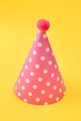 Pink birthday cap on a yellow background. Copy space.