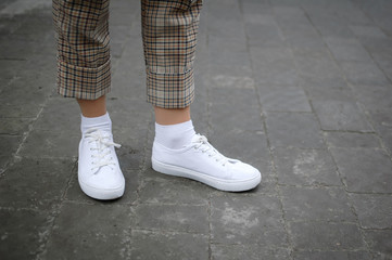 Side view of young women's foot in white sneakers on asphalt background.