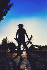 Silhouette of a girl with a bicycle at sunset in the summer