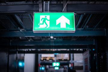 Green emergency exit sign or fire exit sign showing the way to escape with arrow symbol. - obrazy, fototapety, plakaty