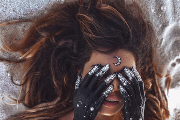 close up of beautiful young woman cover eyes with hands painted black. night and moon concept