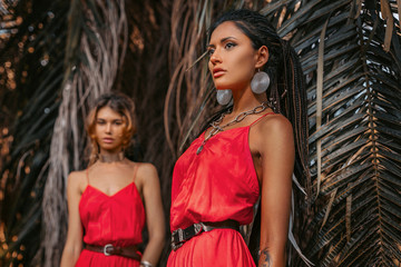 two beautiful young fashionable models in red dresses outdoors at sunset