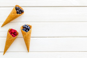 Summer breakfast with fresh berries in waffle cones on white wooden background top view mockup