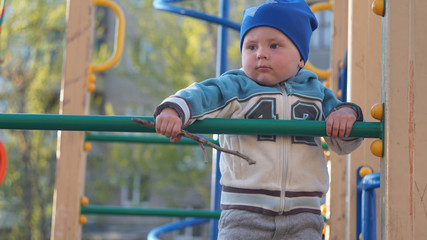 Cute little boy portrait in a blue hat climbs stairs on the playground