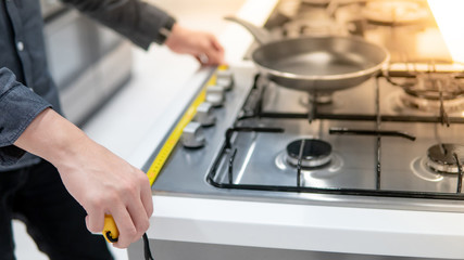 Male hand interior designer using tape measure on gas stove on modern countertop in kitchen showroom. Shopping appliance for domestic kitchen. Home improvement concept
