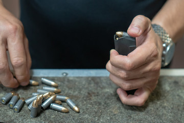 A man in a black T-shirt charges the pistol holder with 9 19 cartridges. The hands of the men charge the gun with ammunition. close-up