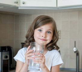 Healthy lifestyle. Portrait of happy smiling young girl with glass. Child drinking fresh water in the kitchen at home, looking at camera. Healthcare. Drinks. Health, beauty, diet concept. Good eating