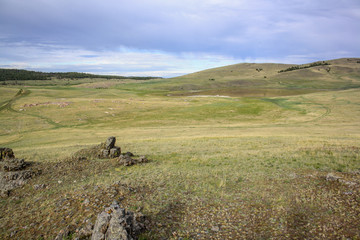 Stones sticking out of the ground and a small lake in the steppe among the yellow grass