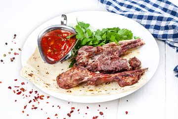 Close up view on served cooked on the grill lamb on bone. shashlik or barbecue meat on pita. Shish kebab, traditional georgian cuisine food. Copy space for design. Meat food with red sauce