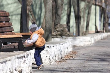 Cute child climbing on the bench in the spring park