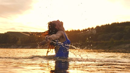 playful girl splashes her long hair in a refreshing summer evening near tropical island with refreshing river water. girl flips back hair. beautiful spray of water in rays of sunset. splash of water