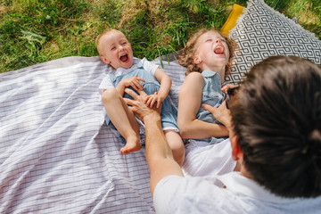 Father tickles his daughters during picnic on grass in the gardens