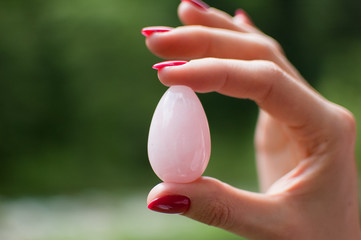 Close up photo of female hand holding a yoni egg. Rose quartz crystal egg on river background....