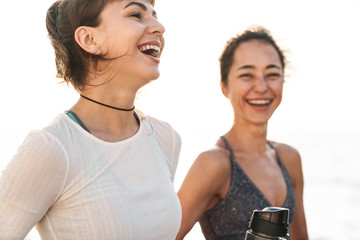 Image of joyful fitness women smiling and standing by seaside in morning