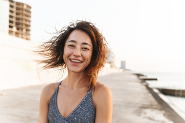 Portrait closeup of beautiful woman smiling and looking at camera while walking by seaside in morning