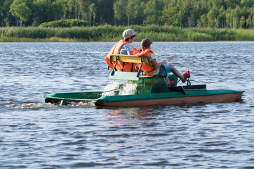 two people in life jackets ride on an iron boat on the river, rear view