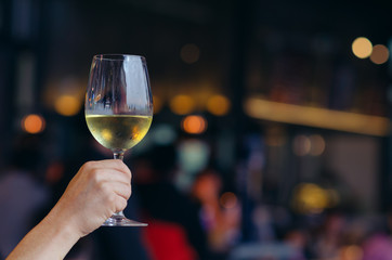 Hand holding a glass of white wine with colorful bokeh light in restaurant.
