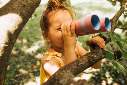 Closeup iamge of cute little girl looking through a binoculars searching for an imagination or exploration in summer day in park. Happy child playing with binocular pretend safari game outdoors.