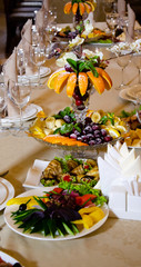 Restaurant vintage, cutlery, glasses on the table, bar, bottles, large candles on a white tablecloth, sliced fruit with powdered sugar