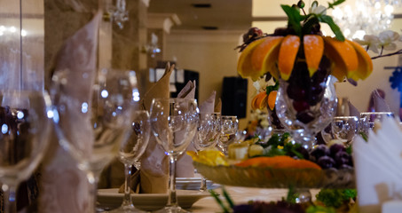 Restaurant vintage, cutlery, glasses on the table, bar, bottles, large candles on a white tablecloth, sliced fruit with powdered sugar