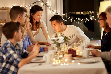 celebration and family concept - man blowing candles on birthday cake at dinner party at home