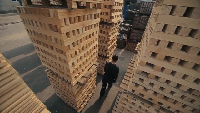 A young worker in uniform walks between wooden pallets in distribution outdoor warehouse. Slow motion. view from above