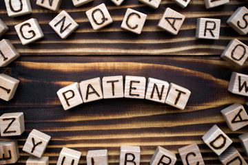 patent composed of wooden cubes with letters, official legal right to make or sell an invention concept, scattered around the cubes random letters, top view on wooden background