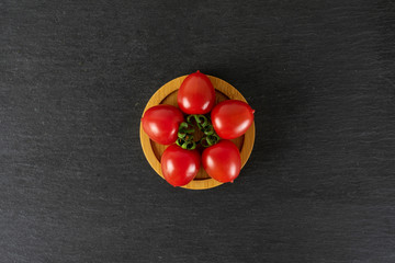 Group of five whole fresh red tomato cherry on a bamboo plate flatlay on grey stone