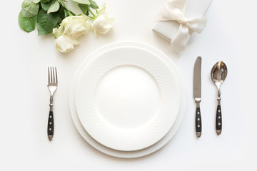 White table setting with rose, gift, dishware, silverware on holiday table. View from above. Romantic and wedding anniversary.