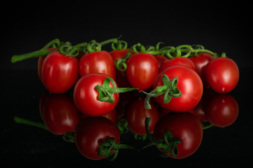 Lot of whole fresh red tomato cherry isolated on black glass