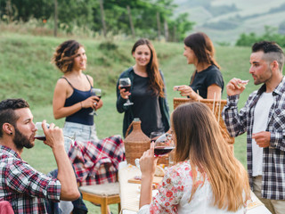 Group of friends during a barbecue in the countryside - Millennials drinking red wine
