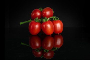 Group of five whole fresh red tomato cherry isolated on black glass