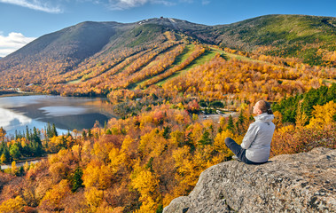 Woman hiking at Artist's Bluff in autumn. View of Echo Lake. Fall colours in Franconia Notch State...