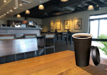 Dark vending coffee in black blank paper cup and plastic lid on wooden table at cafe. 