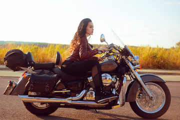 Beautiful brunette in a red leather jacket on a motorcycle in the field. Girl with beautiful hair