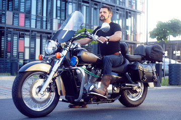Fototapeta na wymiar A man on a motorcycle near the office. Man on a motorcycle takes his girlfriend from work. Biker came to work in the office. The man on the file on the industrial background. A man sits on a motobike.