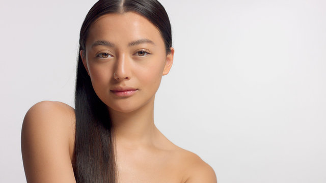 mixed race asian model in studio beauty shoot Model poses to a camera, straight hair combed to right side. Ideal skni and no makeup makeup Head and shoulders crop Watching to the camera