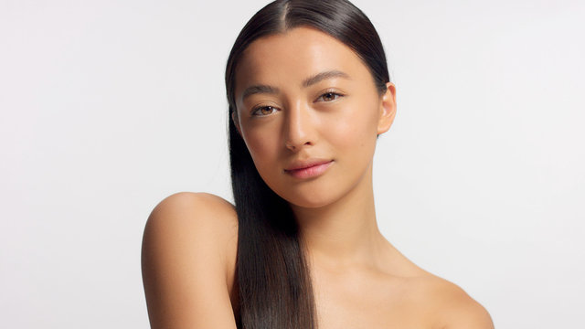 mixed race model with straight hair watching to the camera. Ideal skin, natural glowy makeup. Head and shoulders crop