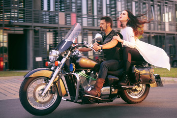 Plakat Couple on the background of the office on a motorcycle. The guy brought his girlfriend to work. Girl in a long white dress on a motorcycle. Couple against the backdrop of an industrial city.