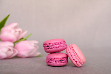 Stack of delicious colorful pink and purple macaron cookies on grey background with flowers. Copy space. 