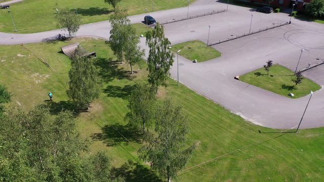 Reverse panning drone footage of some athletes running down a grass trail with trees on the left hand side. Filmed in realtime.