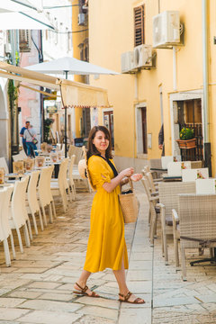 woman in yellow dress walking by resort city street between cafe restaurant tables