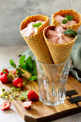Strawberry of ice cream scoops in cones on a light stone or slate table.