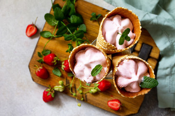 Strawberry of ice cream scoops in cones on a light stone or slate table.