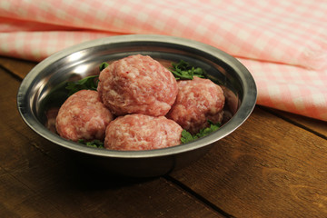 raw mince meat bals in a metal bowl on wooden table top 