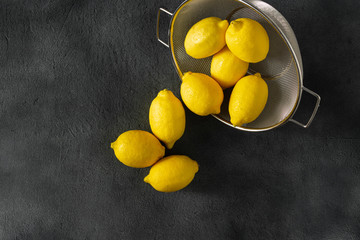 Pile of lemons in colander on a dark background top view