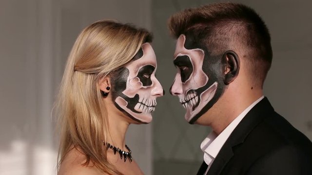 Portrait of a young couple in the Halloween mask. Close-up view of couple of painted halloween holy chracters woman and man. Loving young couple with sugar skull make-up.