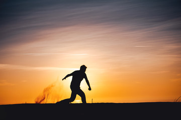 Side view of a active sport athlete man jumping and having fun in wide endless sand dunes at colorful, amazing sunset evening light. Lokken, Lønstrup in North Jutland in Denmark, Skagerrak, North Sea