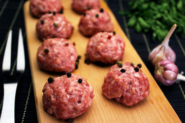 close up raw meatballs with peper beans  on a cutting board on a background of a black bamboo mat with garlic and parsley