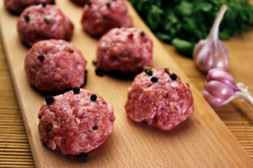 close up raw meatballs with peper beans  on a cutting board on a background of a bamboo mat with garlic and parsley